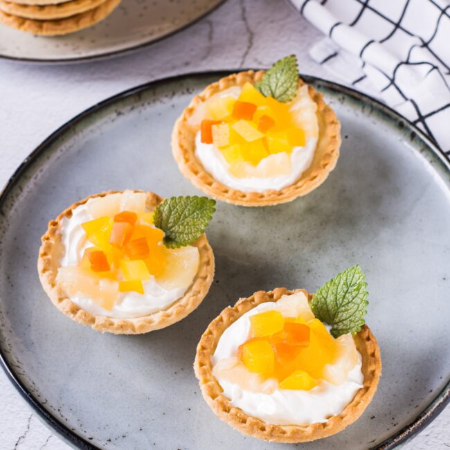 Appetizing tartlet dessert with whipped cream, canned fruit and mint on a plate vertical view